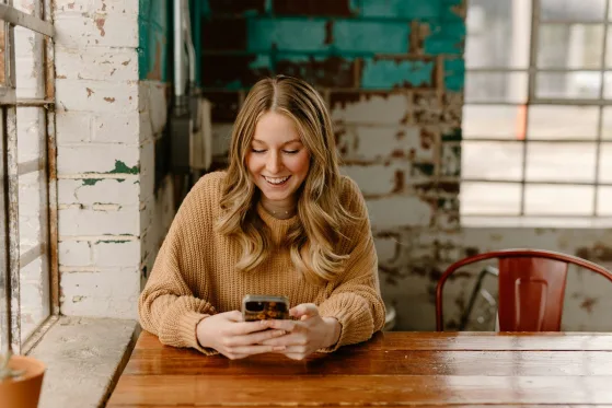 Clienta sonriendo mientras escribe un mensaje en su celular en un café