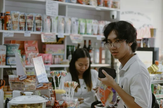 Joven atendiendo su tienda mientras revisa mensajes en el celular
